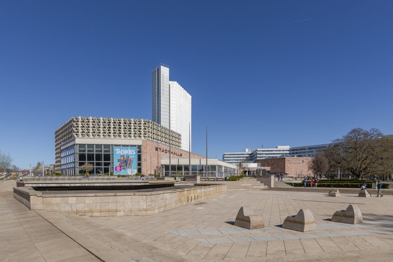 Eine Stadthalle auf einem zubetonierten Platz mit einem Hochhaus dahinter