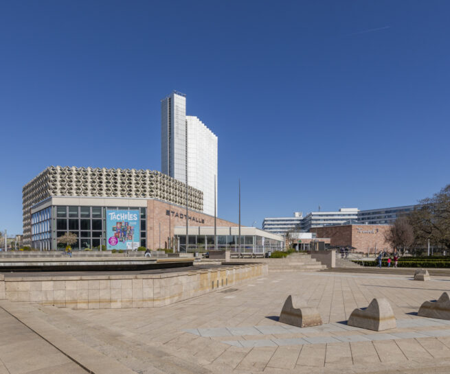 Eine Stadthalle auf einem zubetonierten Platz mit einem Hochhaus dahinter