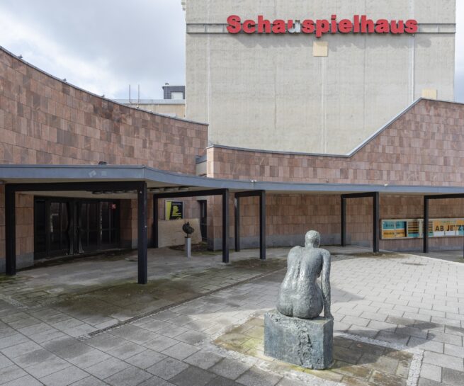 Vorplatz eines Theaters mit einer Skulptur im Vordergrund