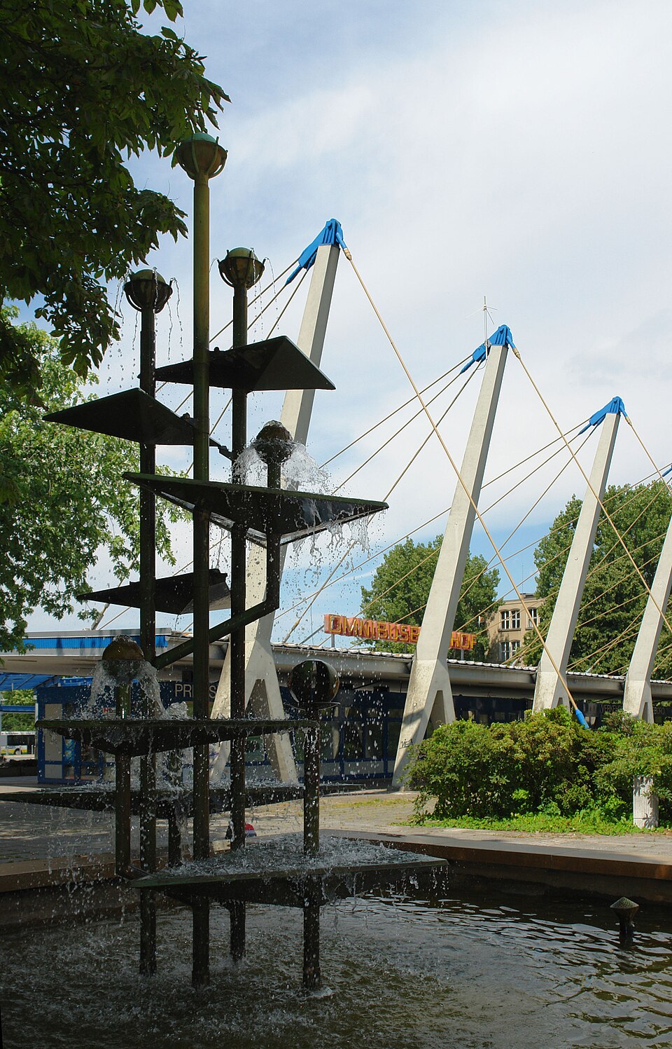 abstrakte Skulptur im Vordergrund. Masten eines Gebäudes im Hintergrund